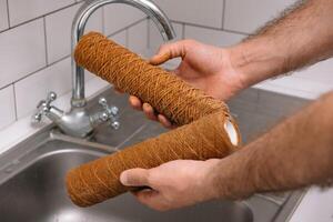 Hand holding dirty water filter cartridge over the sink. Brown coloring. Evidence of contamination of tap water with iron cations. photo