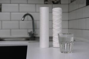 Water filters. Carbon cartridges and a glass on a white kitchen background. Household filtration system photo