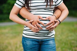 imagen de embarazada Pareja. marido conmovedor su esposa barriga con manos. embarazada mujer al aire libre. foto