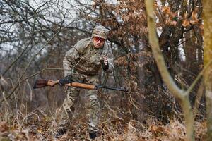 hunting, war, army and people concept - young soldier, ranger or hunter with gun walking in forest. photo