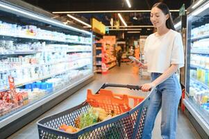 Groceries Shopping. Portrait Of Smiling Happy Woman Leaning On Trolley Cart In Supermarket photo