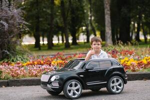 Cute boy in riding a black electric car in the park. Funny boy rides on a toy electric car. Copy space. photo