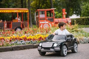 Cute boy in riding a black electric car in the park. Funny boy rides on a toy electric car. Copy space. photo