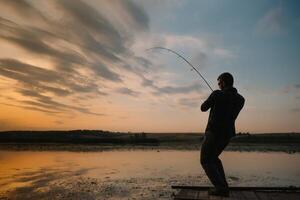 un pescador silueta pescar a puesta de sol. agua dulce pesca, captura de pez. foto