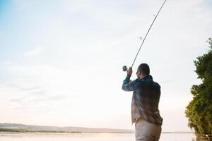 Fisher man fishing with spinning rod on a river bank at misty foggy sunrise. fisher with spinning. spinning concept. photo