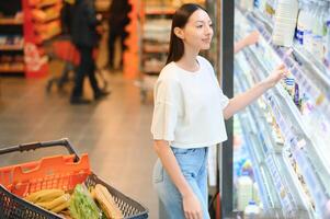 joven sonriente contento mujer 20s en casual ropa compras a supermercado Tienda con tienda de comestibles carro foto