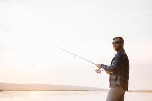 Fisher man fishing with spinning rod on a river bank at misty foggy sunrise. fisher with spinning. spinning concept. photo