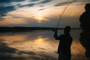 Fisher man fishing with spinning rod on a river bank at misty foggy sunrise. fisher with spinning. spinning concept. photo