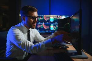 Side view of crypto broker sitting at office table, analyzing market, looking at screen photo