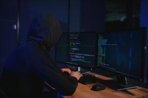 hacker sitting at desk in dark atmosphere. A computer programmer or hacker. Anonymous computer hacker. photo