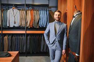 moderno joven hermoso empresario, mirando y elegir clásico traje en el traje tienda foto