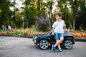 Cute boy in riding a black electric car in the park. Funny boy rides on a toy electric car. Copy space. photo