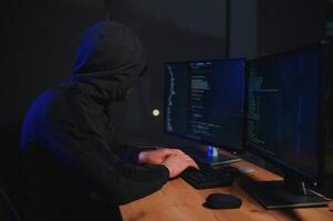 hacker sentado a escritorio en oscuro atmósfera. un computadora programador o hacker anónimo computadora hacker foto