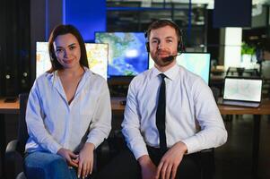 Center of dispatching maintenance. Portrait of cheerful woman and man working via headset microphone while sitting on navigation controller board photo