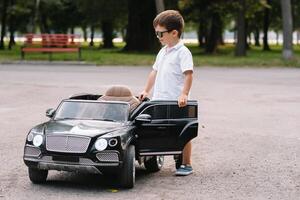 linda chico en montando un negro eléctrico coche en el parque. gracioso chico paseos en un juguete eléctrico coche. Copiar espacio. foto