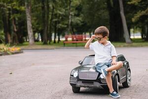 Cute boy in riding a black electric car in the park. Funny boy rides on a toy electric car. Copy space. photo