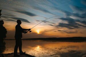 un pescador silueta pescar a puesta de sol. agua dulce pesca, captura de pez. foto