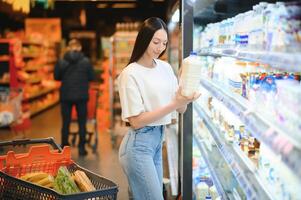 sonriente contento mujer disfrutando compras a el supermercado, ella es propensión en un lleno carro foto