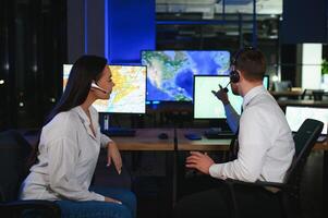 Center of dispatching maintenance. Portrait of cheerful woman and man working via headset microphone while sitting on navigation controller board photo