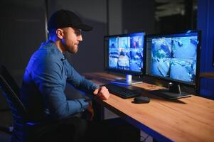 Rear view of security system operator looking at CCTV footage at desk in office photo