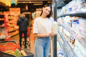 joven sonriente contento mujer 20s vestir casual ropa compras a supermercado Tienda comprar escoger Leche foto