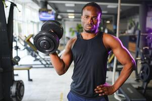 Young man strengthening biceps with dumbbell in gym photo