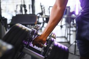 Close-up man grabs a heavy dumbbell in gym with his hand. Concept lifting, fitness photo