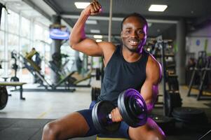 joven hombre fortalecimiento bíceps con pesa en gimnasio foto