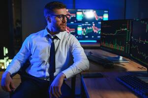 Side view of crypto broker sitting at office table, analyzing market, looking at screen photo