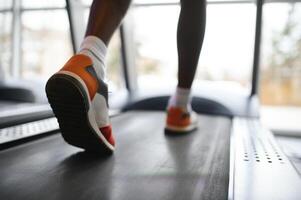 Back view of unrecognizable male legs running on treadmill in gym. photo