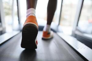 Back view of unrecognizable male legs running on treadmill in gym. photo