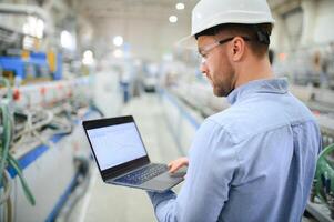 Side view of technician or engineer with headset and laptop standing in industrial factory photo