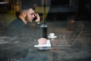 Young businessman talking on mobile phone while working on laptop in cafe. photo