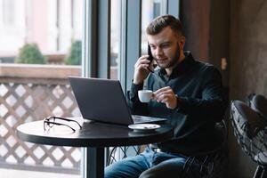 joven empresario hablando en móvil teléfono mientras trabajando en ordenador portátil en café foto