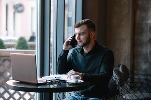 Young businessman talking on mobile phone while working on laptop in cafe. photo