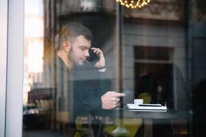 Young businessman talking on mobile phone while working on laptop in cafe. photo