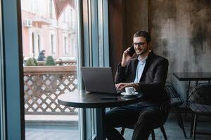 Young businessman talking on mobile phone while working on laptop in cafe. photo