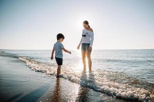 Mother and son playing on the beach at the sunset time. Concept of friendly family photo