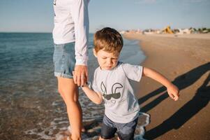 Mother and son playing on the beach at the sunset time. Concept of friendly family photo