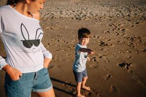 Mother and son playing on the beach at the sunset time. Concept of friendly family photo