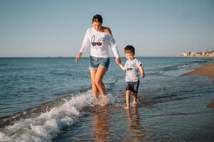 Mother and son playing on the beach at the sunset time. Concept of friendly family photo