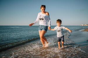 madre y hijo jugando en el playa a el puesta de sol tiempo. concepto de simpático familia. foto