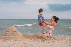 Mother and son playing on the beach at the sunset time. Concept of friendly family photo