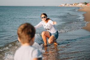 madre y hijo jugando en el playa a el puesta de sol tiempo. concepto de simpático familia. foto