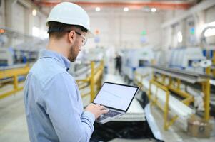 Side view of technician or engineer with headset and laptop standing in industrial factory photo