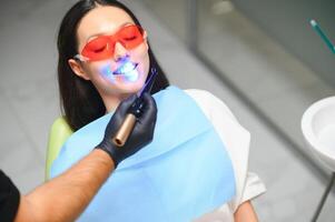 joven mujer consiguiendo dental relleno el secado procedimiento con curación uv ligero a dental clínica foto