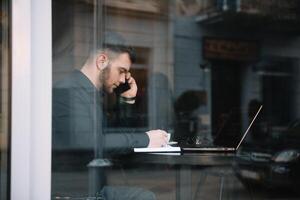 Young businessman talking on mobile phone while working on laptop in cafe. photo