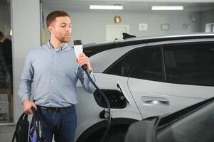 barba hombre molesto un nuevo cargando cable con un coche cargando estación a el motor concesión. concepto de comprando eléctrico vehículo. inteligente ecológico vivo foto