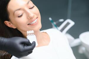 dentista comprobación y seleccionando color de joven mujer dientes foto