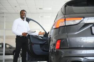 young african american car dealership principal standing in vehicle showroom photo